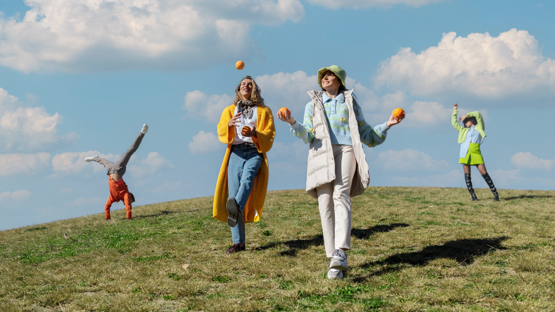 two-female-friends-playing-with-oranges-other-two-dancing-outdoor-field